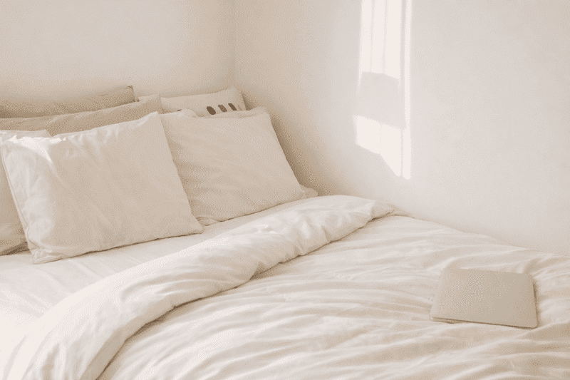 Frequência correta de lavagem de toalhas, lençóis e cobertas 3 Cama com lençóis brancos e toalha dobrada simbolizando a frequência correta de lavagem de toalhas e a importância da higiene no quarto.