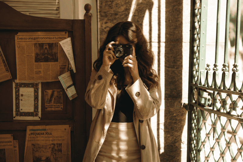 Hobbies criativos para adolescentes tímidas 3 Jovem mulher fotografando com câmera vintage em ambiente iluminado pelo sol, com estética aconchegante e tons quentes, representando hobbies criativos para adolescentes ligados à fotografia.